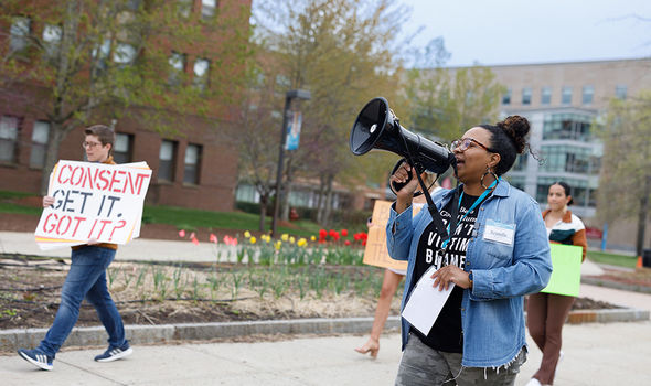 A student organizer speaks through a megaphone as students march in a Take Back the Night rally; in the background, a person holds a sign that says, &quot;Consent: Get it. Got It?&quot;