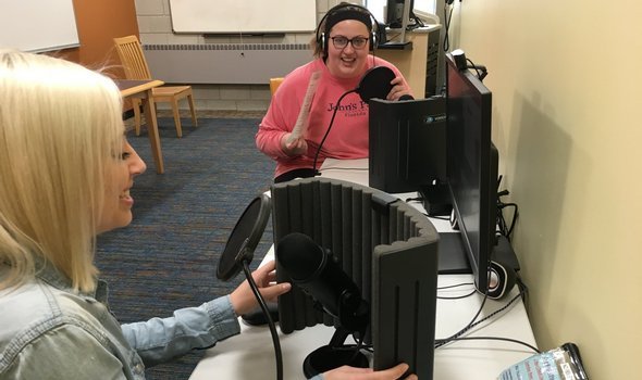 2 students at microphones with headphones on creating a podcast