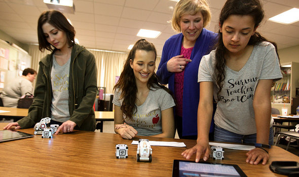 Education professor with students wearing Teacher Bootcamp t-shirts using ipads and small robots