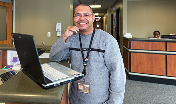 BSU Social Work graduate at work posing with his open laptop standing at a reception desk