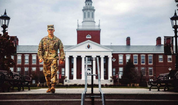 a student in military fatigues walks on BSU's Boyden quad with Boyden Hall in background