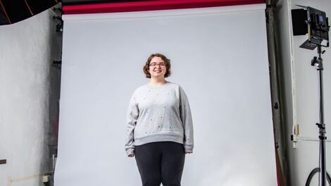 Mackenzie Cobb stands in front of a white backdrop illuminated by lights.