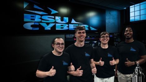 Four students give thumbs up while standing in front of a screen with the BSU Cyber logo.
