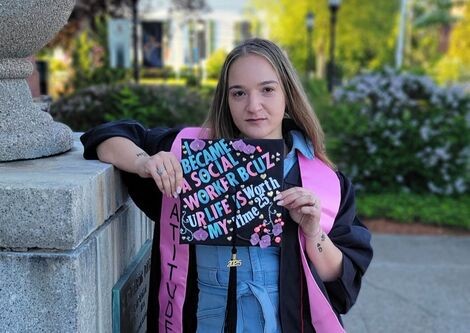 A woman stands holding her graduation cap