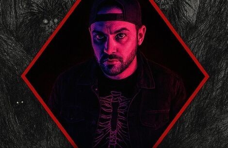 A man wears a baseball cap backwards staring at camera with menacing look 