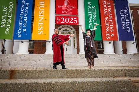A woman stands on stairs with her hands up in the air, smiling while a man stands next to her also smiling