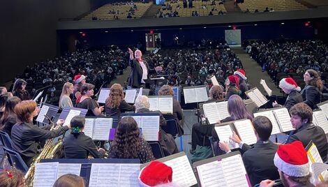 Musicians sit on a stage and look up at the conductor 