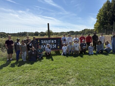A group stands in front of a Share the Harvest Sign
