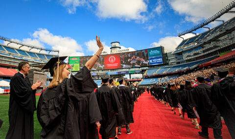 As BSU graduates process into Gillette Stadium, a graduate waves to the crowd in the stands