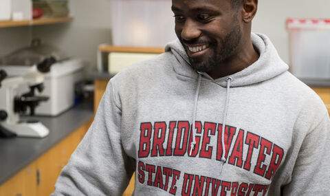 a male student wearing a light gray BSU hoodie smiling in biology lab
