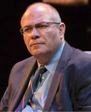 Dr. Francisco Alatorre balding with short gray hair wearing brown rim glasses a light blue button down shirt, navy blue tie and blazer