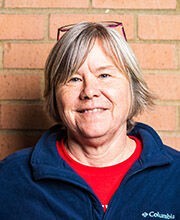 headshot photo of Kathy Bailey with short gray hair wearing a red top under a navy blue zip up fleece