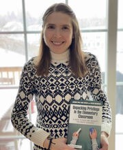 Dr. Jacquelynne Boivin smiling with long light brown hair and wearing a black and white sweater. She is holding her book titled Unpacking Privilege in the Elementary Classroom