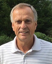 Headshot photo of Gary Calhoun with short gray hair wearing a white polo shirt with vertical gray stripes on it