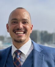 Dr. Aaron Coleman smiling with very short brown hair, mustache and goatee. He is wearing a blue blazer and vest over a white button down shirt with blue tie