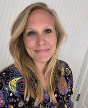 Dr. Samantha Ewart smiling with long dirty blonde hair wearing a v-neck top with black background and colorful design