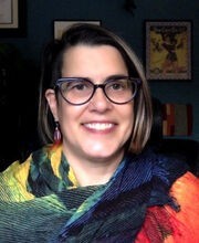 Dr. Kimberly Fox smiling with straight, medium length highlighted brown hair. She's wearing black rimmed glasses and a red, yellow, blue and green wrap