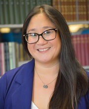 Dr. Holly Grant-Marsney smiling with long straight dark brown hair and wearing black rim glasses, a royal purple blazer and a white v-neck blouse