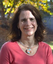Dr. Lynn Hansberry Mayo smiling with medium length dark brown wavy hair and wearing a salmon v-neck top