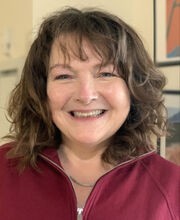 Dr. Jeanne Ingle smiling with shoulder length wavy dark brown hair and wearing a maroon zip up top