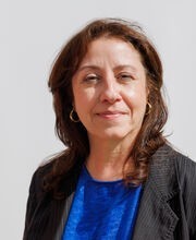 Dahri McFaline smiling with long wavy brown hair and wearing a black blazer over a royal blue top