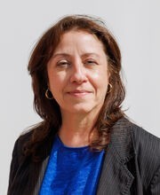 Dahri McFaline smiling with long wavy brown hair and wearing a black blazer over a royal blue top