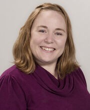 Dr. April Megginson smiling with medium length red hair and wearing a cowl neck raspberry colored sweater