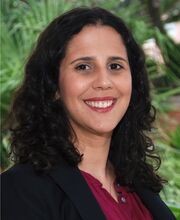headshot photo of Dr. Rachel Navarre smiling with long dark brown curly hair, wearing a black blazer over a maroon button down top