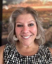 Heather Pacheco-Guffrey smiling with shoulder length gray hair and wearing a sleeveless black and white blouse