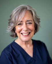 Beth Anne Young smiling with short wavy gray hair and wearing a v-neck navy blue blouse