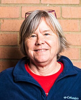 headshot photo of Kathy Bailey with short gray hair wearing a red top under a navy blue zip up fleece