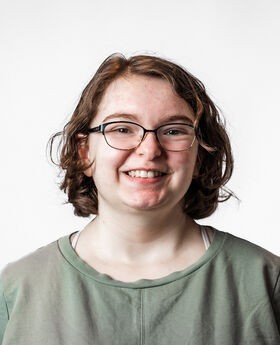 Mackenzie Cobb, '26 with medium length brown wavy hair wearing black rim glasses and a green top