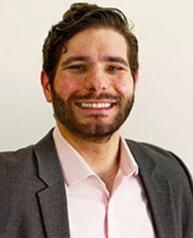 headshot photo of Dr. Kevin Duquette smiling with brown hair, mustache and beard wearing a gray blazer over a pink button down shirt
