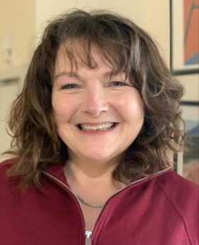 Dr. Jeanne Ingle smiling with shoulder length wavy dark brown hair and wearing a maroon zip up top