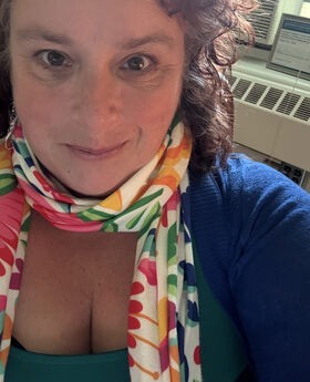 Bridget Lehane smiling with medium length curly brown hair and wearing a blue sweater and colorful scarf