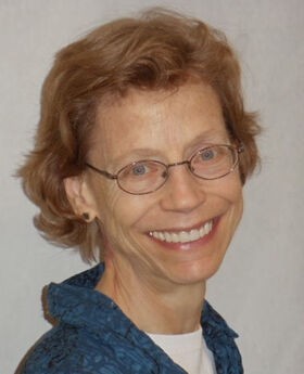Dr. Margaret Lowe smiling with short wavy red hair wearing gold rim glasses and a blue top