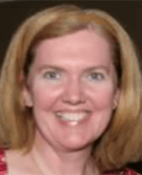 Kelly McMorrow smiling with medium length dirty blonde hair wearing a brown headband and a pink patterned top