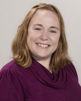 Dr. April Megginson smiling with medium length red hair and wearing a cowl neck raspberry colored sweater