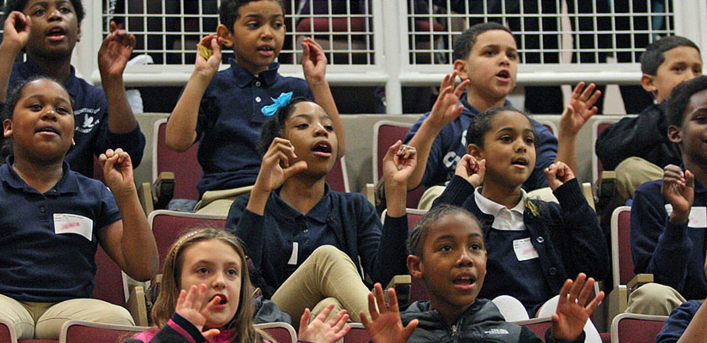 A group of children sitting in BSU Moakley Auditorium singing